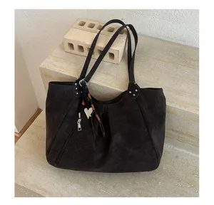 Detail view of dark slouchy shoulder tote bag with heart charm and textured leather.