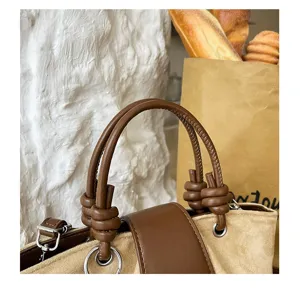 Handbag detail view showing brown suede texture, knotted handle design, and silver metal hardware.
