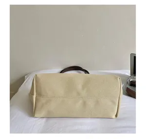 Bottom detail of a minimalist beige canvas tote bag with brown handles, showing neat stitching.