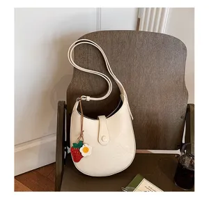 Detailed view of minimalist white saddle shoulder bag with cute strawberry charm.