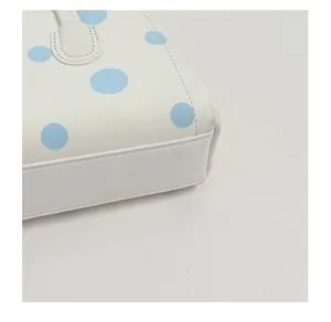 Primer plano detallado de bolso de cuero blanco con estampado de lunares azules y costuras.