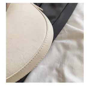 White PU leather underarm bag detail view, simple fashion saddle bag craftsmanship display.