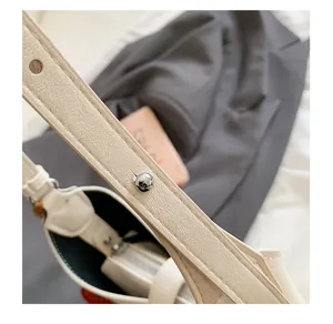 Detail view of minimalist off-white leather underarm bag strap with silver metal rivet.