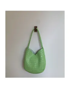 Close-up detail view of light green woven leather underarm shoulder bag on wall.