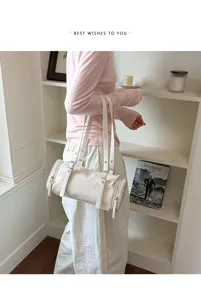 Vista detallada de un elegante bolso de hombro cilíndrico blanco con correas dobles.