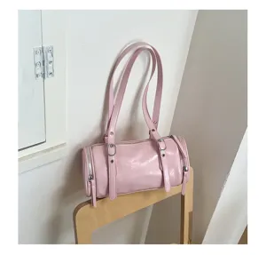Detalle bolso bandolera cilíndrico rosa, estilo retro con hebillas metálicas finas.