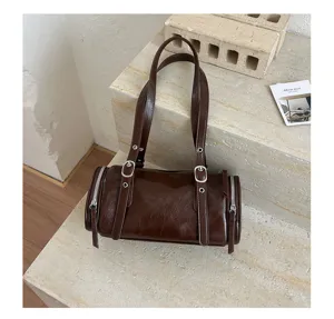 Detalle de bolso cilíndrico de charol marrón, bolso retro de hombro con hebillas metálicas.