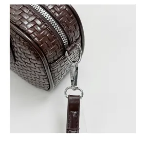 Close-up detail of dark brown woven leather handbag zipper and metal hardware strap.