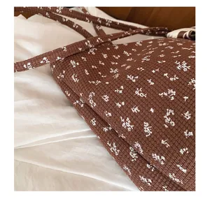Detailopname van een bruine schoudertas met bloemenprint, zachte textuurstof en slanke bandjes.