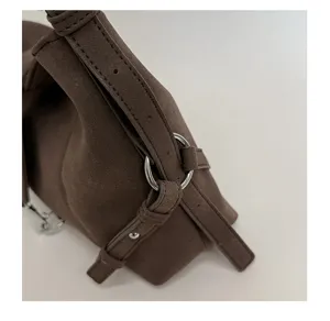 Detailaufnahme der braunen Wildleder-Schultertasche, Metallring-Riemen, minimalistisches Design.