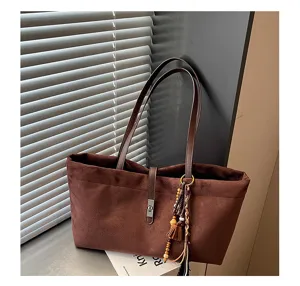 Primer plano de un bolso tote de ante marrón con asas dobles y colgante de borla elegante.