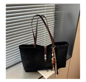 Detalle de primer plano de bolso tote de ante negro con asas de cuero marrón y borlas.