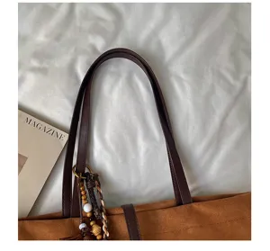 Primer plano del asa del bolso tote de ante marrón con colgante de cuentas y revista.