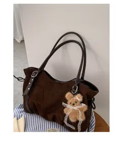 Detail view of brown suede tote bag featuring a cute plush bear pendant with lace bow.