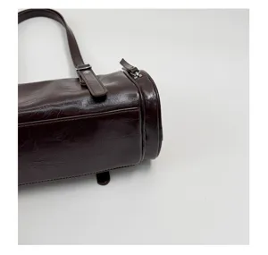 Detalle de bolso de hombro cilíndrico marrón oscuro, diseño retro de bolso bombo con cremallera.