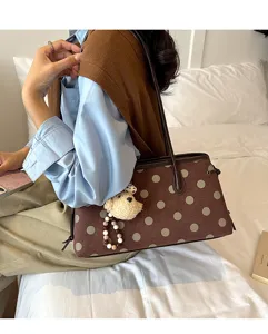 Detailed view of brown suede shoulder bag with polka dots and cute bear pendant in daily scene.