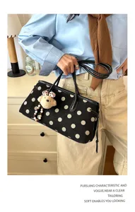 Detail shot of black suede tote bag with white polka dots, leather handles and cute bear charm.