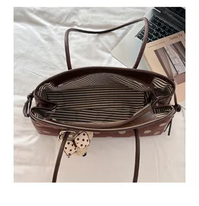 Detailed view of brown suede polka dot shoulder bag with striped lining and cute bow charm.