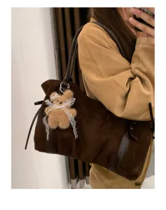 Brown suede underarm shoulder bag detail view featuring a fluffy plush bear pendant.
