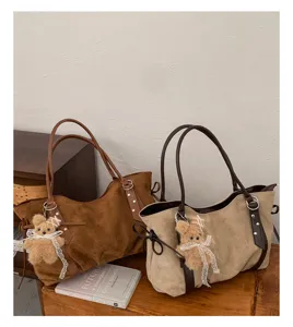 Suede tote bag detail showing large capacity, soft texture and cute bear pendant design.