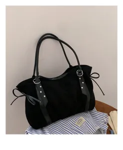 Black suede shoulder bag detail, featuring dual straps, metal rings, and chic side bows.