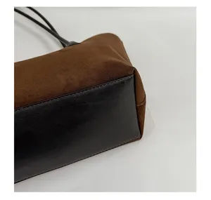 Detail shot of brown suede and black leather shoulder bag bottom showing fine stitching.