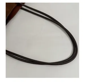 Close-up of brown suede tote bag handle showing fine leather strap texture and stitching.