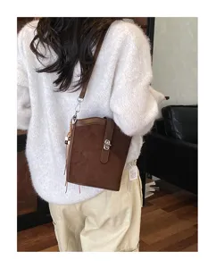 Primo piano della borsa a secchiello in camoscio marrone con chiusura in metallo e nappe.