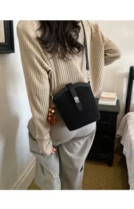 Dettaglio di una borsa a secchiello nera indossata a tracolla con chiusura elegante.