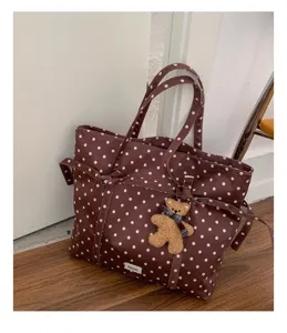 Detalle de bolso tote de lona con lunares marrones y colgante de osito de peluche.