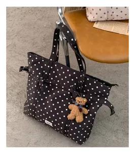 Primer plano detallado de un bolso tote de lona con lunares marrones y llavero de oso.