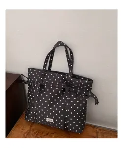 Vista detallada del bolso tote de lona negra de lunares con un elegante lazo decorativo.