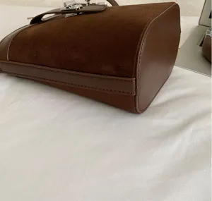 Primo piano dettagliato di un'elegante borsa a secchiello in camoscio marrone con fibbia.