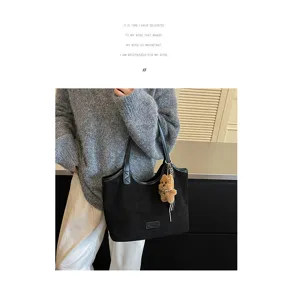 Detailed view of the black suede tote bag with stylish bear pendant and shoulder straps.