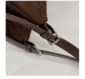 Gros plan sur la sangle de sac en suède marron avec une boucle en métal élégante.