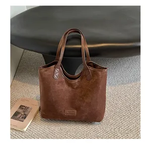 Close-up of a brown suede tote bag showing soft texture, dual handles and minimalist style.