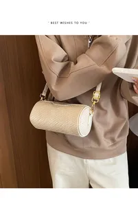 Close up of a woven cylinder shoulder bag with metal hardware details in neutral beige tone.