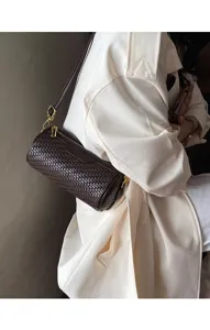 Close-up detail of the retro brown woven cylindrical shoulder bag worn with a white coat.