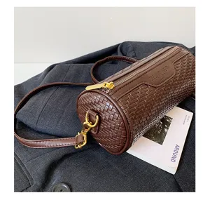 Close-up view of dark brown woven cylinder shoulder bag with gold zipper and stylish prop book.