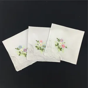 Detailansicht eines weissen Baumwolltaschentuchs mit zarter Blumenstickerei und Spitzenkanten.