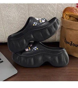 Detailed close-up shot of stylish black platform slippers with floral charms on a desk.