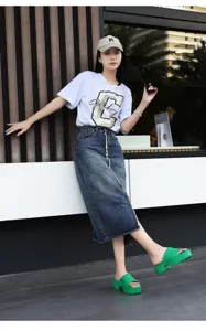 Detailed shot of trendy green platform slide sandals worn by a model in an urban street scene.