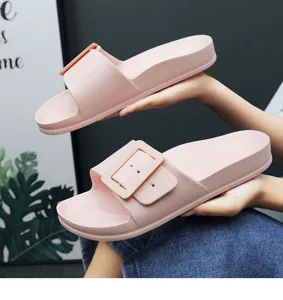 Detailed view of pink thick-sole slide sandals with a large square buckle, hand model shot.