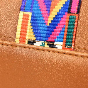 Detailopname van een dameshandtas in bruin leer en met gekleurde geweven etnische riem.