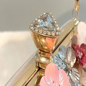 Close-up detail showing the sparkling rhinestone clasp and elegant floral appliques on the clutch.