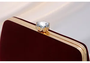 Burgundy velvet evening clutch bag detail, featuring gold metal frame and sparkling crystal.