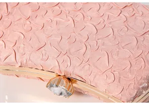 Elegant pink evening clutch bag detail showing textured fabric, golden metal frame, and crystal clasp.