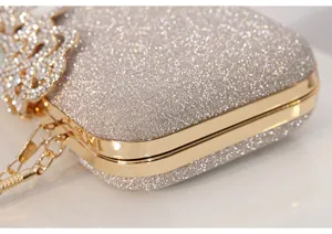 Detalle del bolso de noche brillante con marco dorado metálico y elegante broche de pedrería.