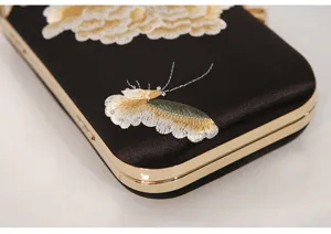 Black satin evening bag detail with gold metal frame and delicate embroidered flowers.
