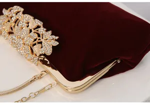 Close-up detail of burgundy velvet evening clutch bag with rhinestone floral clasp and gold chain.